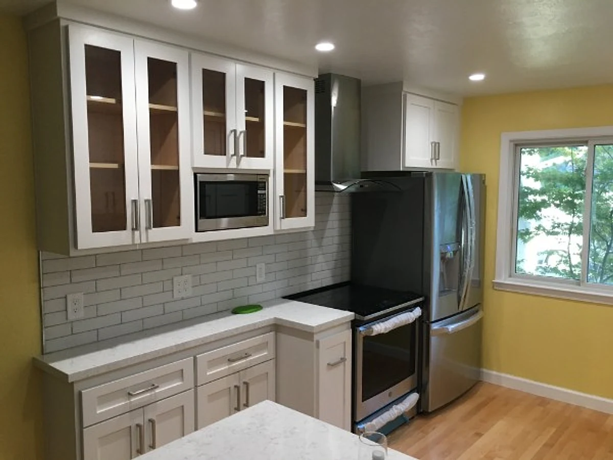 White kitchen cabinets with glass-front uppers, gray subway tile and stainless appliances